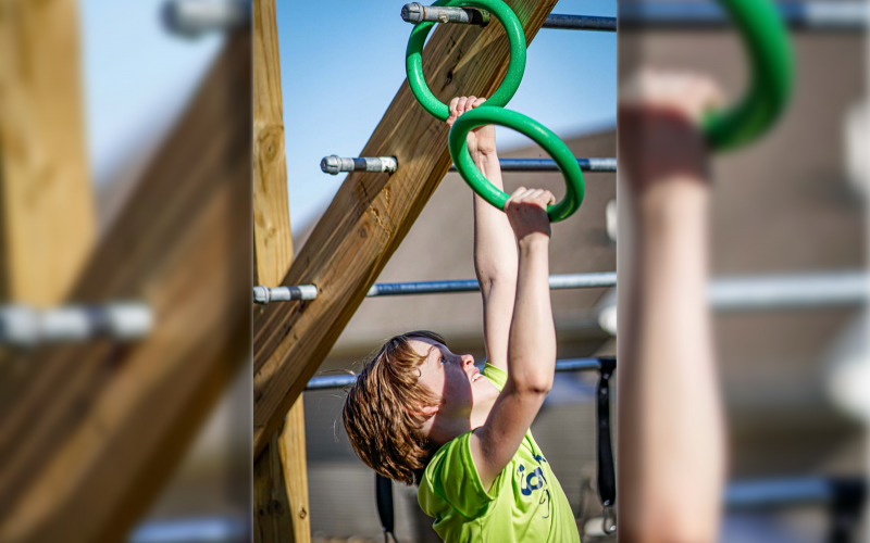 Dylan climbs and obstacle by alternating rings over poles.